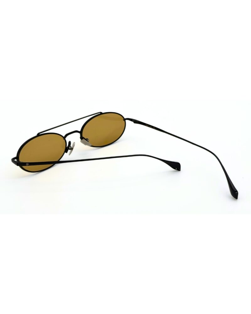 Homme au style urbain portant des lunettes de soleil BLUE EYES noires, monture fine à double pont et verres ambre clair.