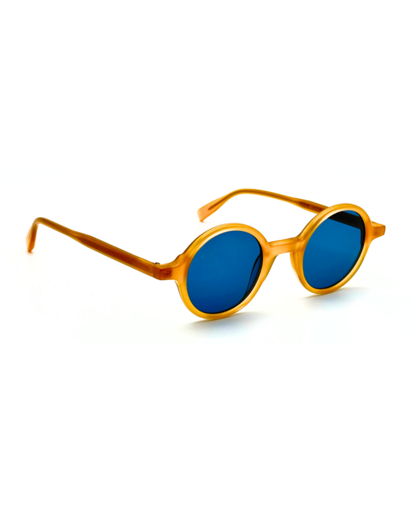 Lunettes de soleil rondes en acétate jaune miel Gigi Studios Greta avec verres bleus sous angle de trois quarts.
