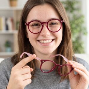 Présentation en main des lunettes de vue enfant Prestigio montrant la face bordeaux et les branches rose translucide