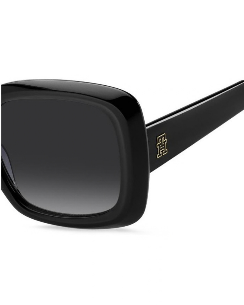 Gros plan sur le logo monogramme TH doré incrusté sur la branche en acétate noir des lunettes Tommy Hilfiger TH 2208/S